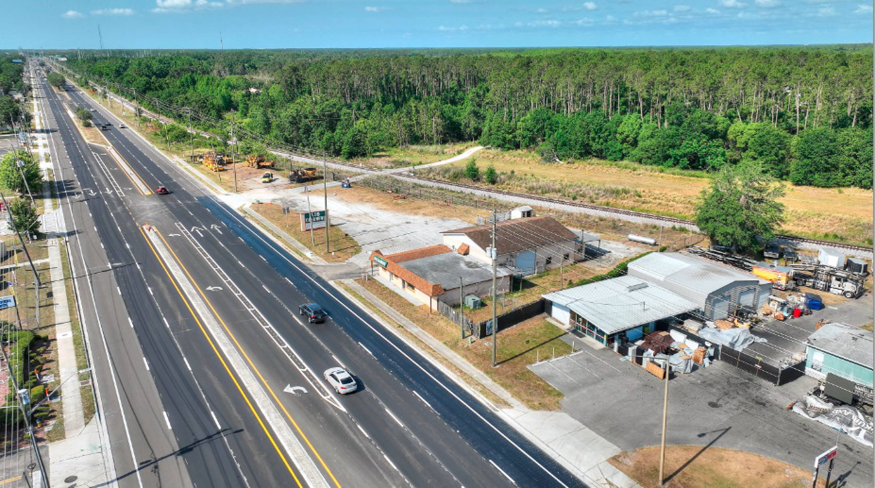 An angled aerial shot showing the significant road frontage of the property and existing buildings along the multi-lane Land O' Lakes Blvd.