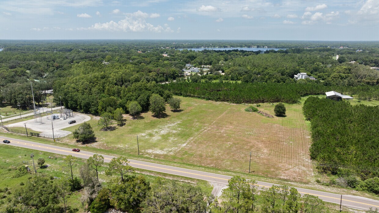 Wide panoramic aerial showing the 4.7-acre lot, surrounding wooded areas, and nearby lakes in the background.